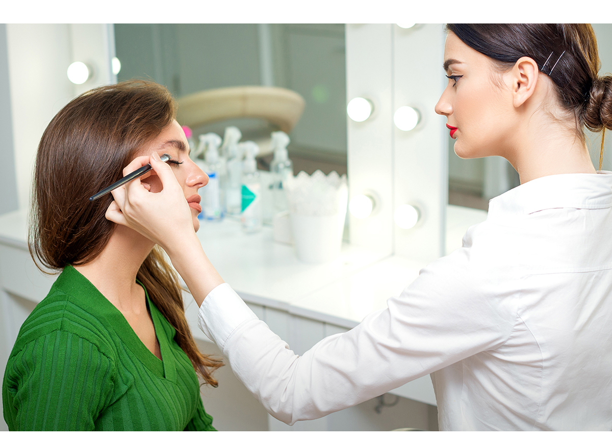 Makeup artist applies eyeshadow powder on eyes of young caucasian woman by brush tool in beauty salon